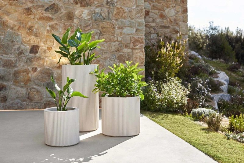 Kremowe okrągłe donice Vondom Gatsby z roślinami przy kamiennym murze w ogrodzie